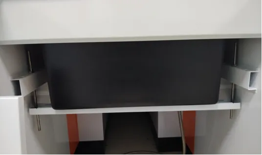 Close-up of a black plastic sink basin mounted under a countertop on a white metal support frame