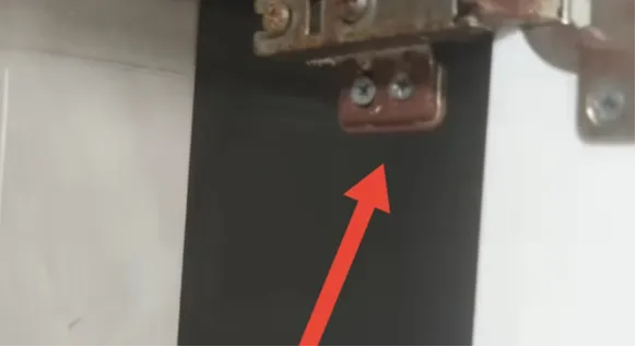 Close-up of a screwed metal hinge on black and white steel laboratory bench paneling with red arrow