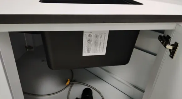 Under-cabinet detail of all-steel laboratory bench showing black sink, drain pipes and door hinge