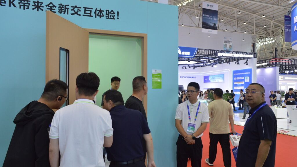 Hospital construction delegates gathering around Pengchi's smart medical cleanroom door demonstration at CHCC2025 while a Pengchi engineer in a branded white polo explains the exhibit on a busy red-carpeted aisle