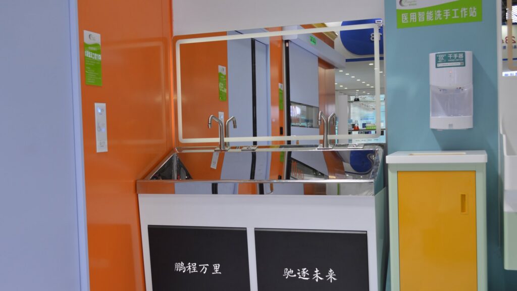Double-station mirror-polished 304 stainless steel surgical handwashing sink with gooseneck sensor faucets and a large backlit mirror displayed at the CHCC2025 exhibition