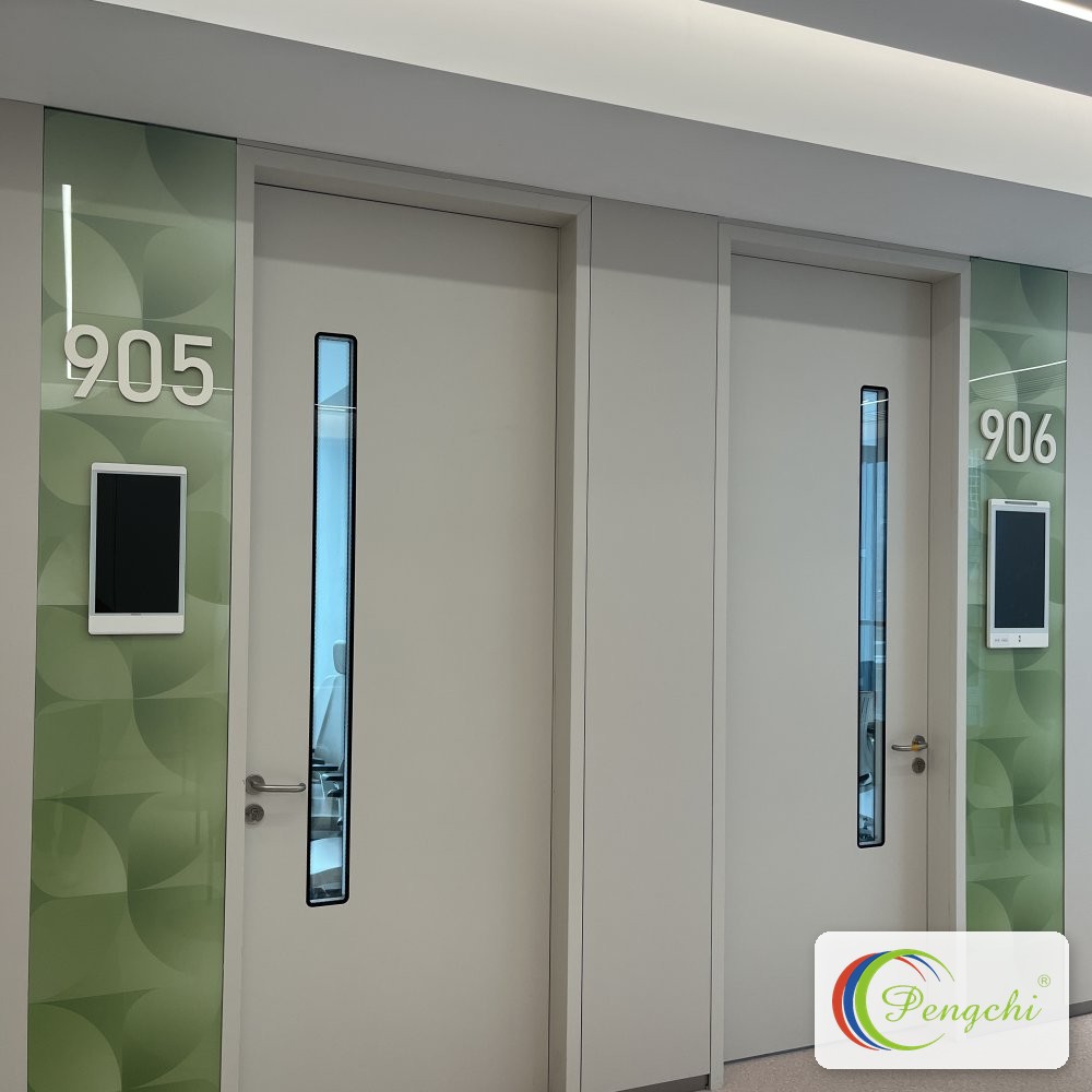 Row of color-coded Pengchi medical doors with narrow glazing and digital room panels along the inpatient corridor at Shenzhen Aier Eye Hospital headquarters.