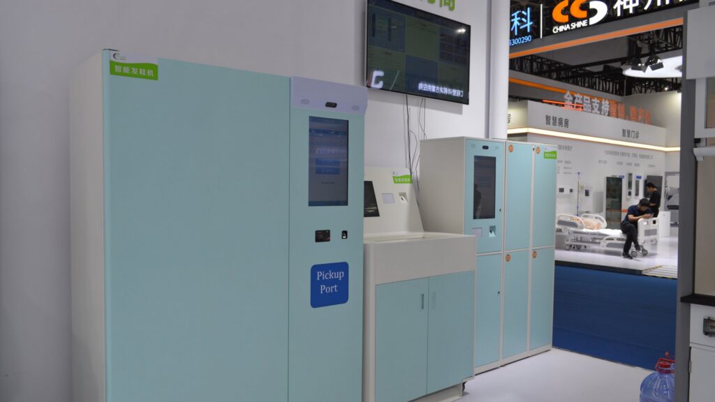 Row of Pengchi intelligent medical storage cabinets with touchscreen interfaces, electronic access control, pickup port and numbered locker compartments on display at CHCC2025, with a smart ward exhibition area behind
