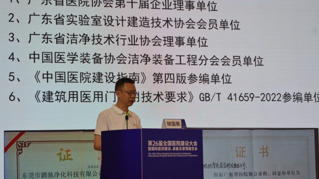 Pengchi representative Hu Guopeng speaking at the blue CHCC2025 conference podium, with the screen behind listing industry credentials including hospital association board memberships and participation in compiling the GB/T 41659 technical requirements for medical doors